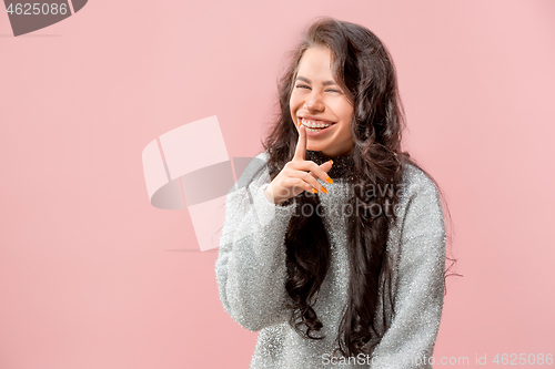 Image of The young woman whispering a secret behind her hand pink background