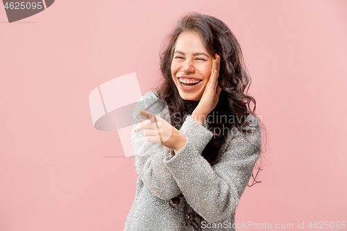 Image of The young woman whispering a secret behind her hand pink background