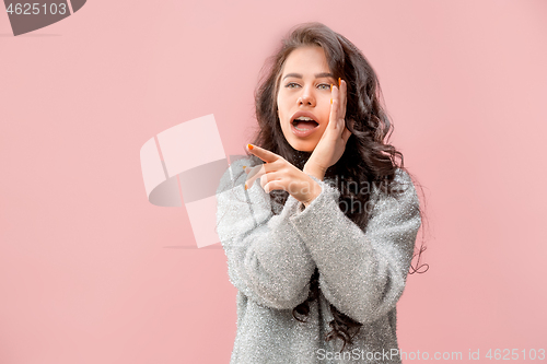 Image of The young woman whispering a secret behind her hand pink background