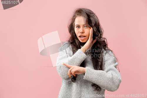 Image of The young woman whispering a secret behind her hand pink background