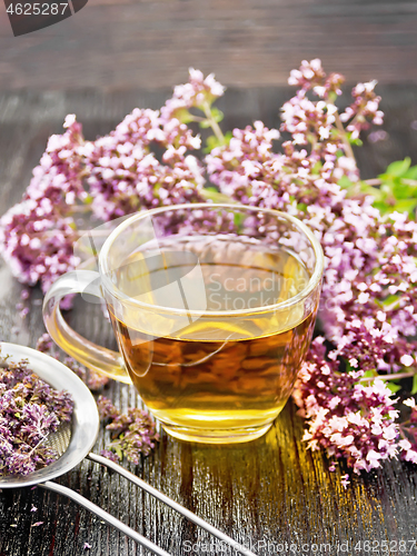 Image of Tea of oregano in cup with strainer on dark wooden board