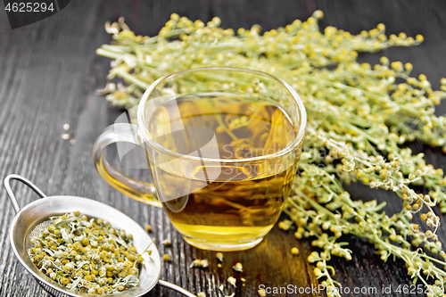 Image of Tea of gray wormwood in glass cup with strainer on wooden board