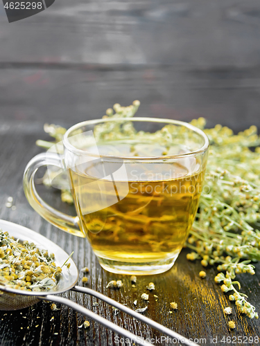 Image of Tea of gray wormwood in glass cup with strainer on dark board