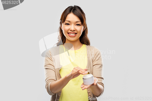 Image of happy young asian woman holding jar of moisturizer