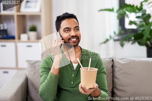 Image of smiling indian man eating takeaway food at home