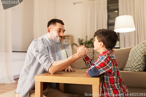 Image of happy father and little son arm wrestling at home