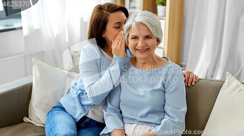 Image of adult daughter whispering to senior mother at home