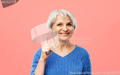 Image of smiling senior woman pointing finger up over pink