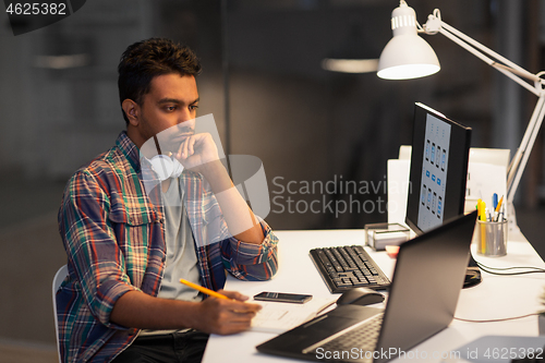 Image of creative man with laptop working at night office