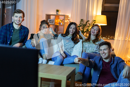 Image of happy friends watching tv at home in evening