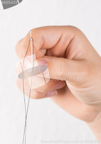 Image of Detail of hand holding needle with thread on white background