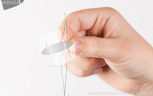 Image of Detail of hand holding needle with thread on white background