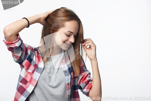 Image of Smiling teen girl touching her hair looking down, studio portrait