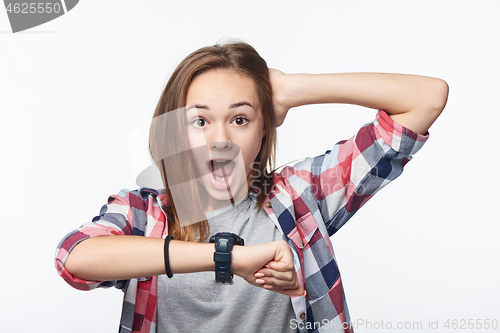 Image of Shocked teenage girl holding hand with wrist watch and looking at camera shouting