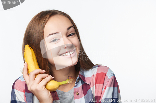 Image of Teen girl holding banana like a phone, looking at camera smiling