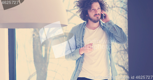 Image of young man drinking coffee and using a mobile phone  at home