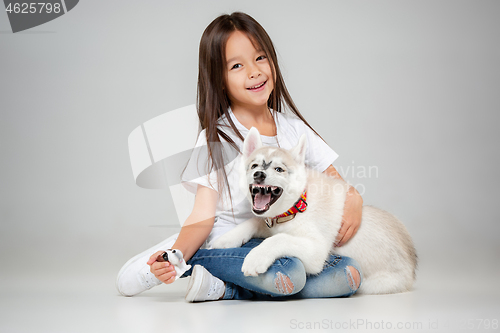 Image of Portrait of a joyful little girl having fun with siberian husky puppy on the floor at studio