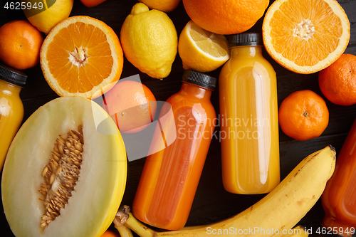 Image of Mix of orange and yellow colored fruits and juices on black wooden background