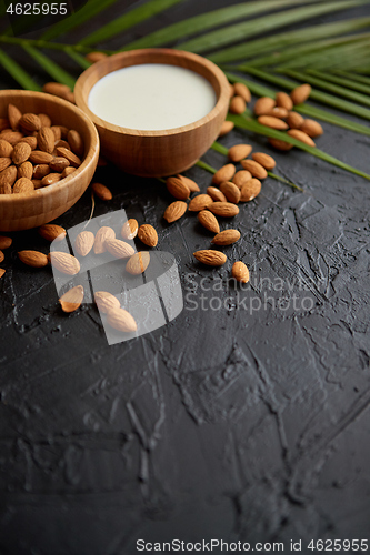 Image of Amond seeds in wooden bowl, fresh natural milk placed on black stone background