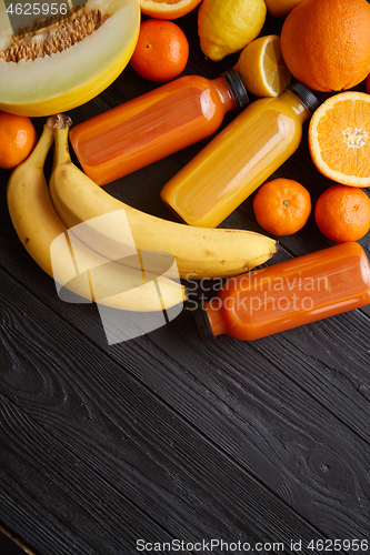 Image of Yellow and orange fruits and botteled juices placed on black wooden background