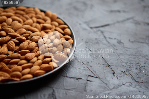 Image of Whole almond nuts in black plate placed on black stone table