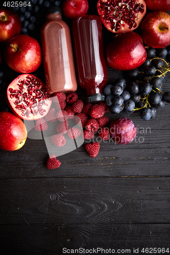 Image of Various fresh red, purple black fruits. Mix of fruits and bottled juices on black