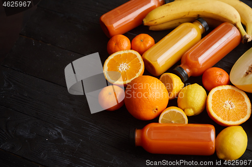 Image of Yellow and orange fruits and botteled juices placed on black wooden background