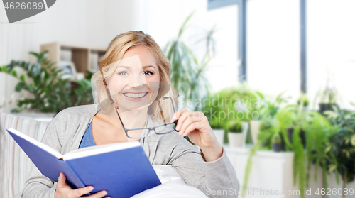 Image of smiling woman reading book and sitting on couch