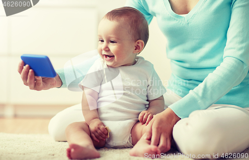 Image of happy mother showing smartphone to baby at home