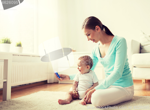 Image of happy mother showing smartphone to baby at home