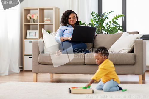 Image of mother using laptop and baby playing toy blocks