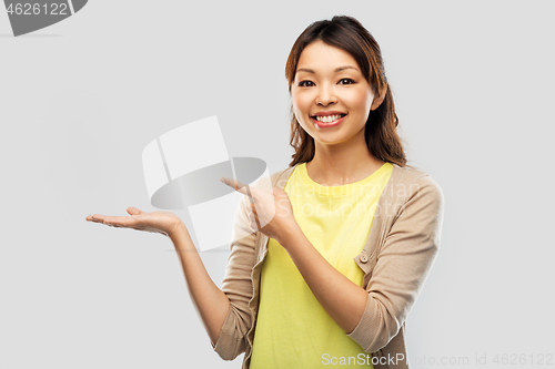 Image of happy asian woman holding something on hand