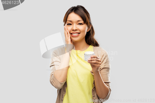 Image of young asian woman applying moisturizer to her face