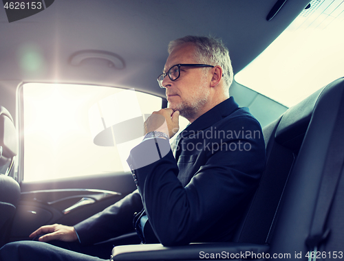 Image of senior businessman driving on car back seat