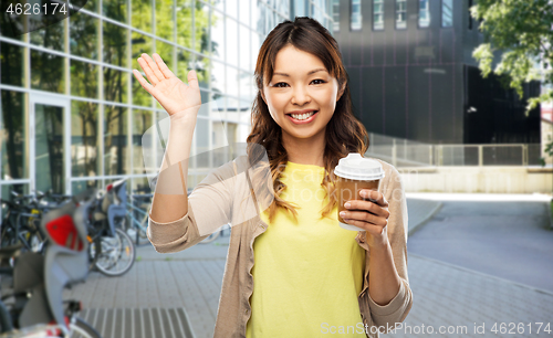 Image of asian woman with coffee waving hand on city street