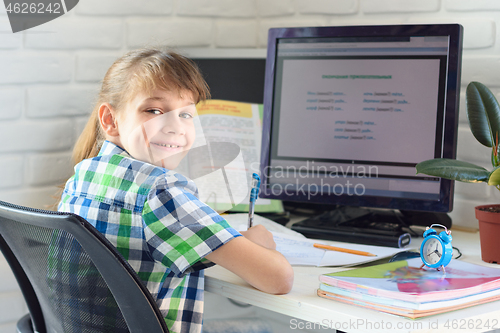 Image of A satisfied child sits at a computer table and looks into the frame