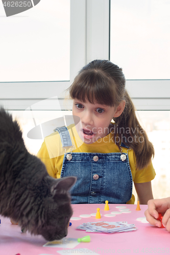 Image of The girl was very surprised when a cat jumped onto the table with a board game