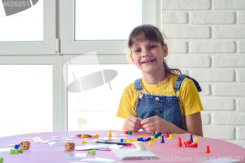 Image of Cheerful girl plays board games at the table and looked into the frame