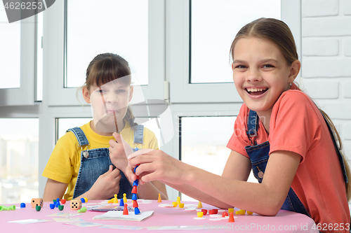 Image of One girl laughs cheerfully, the other makes faces, children play a board game
