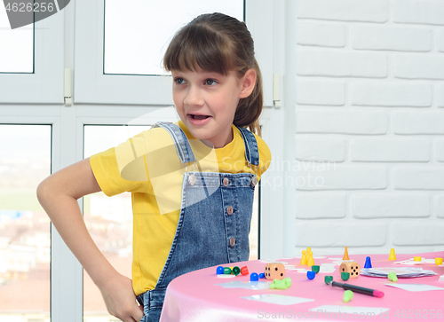 Image of Cheerful girl with a funny face sits at a table playing a board game