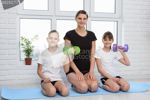 Image of Family poses on the floor in sportswear with dumbbells at home