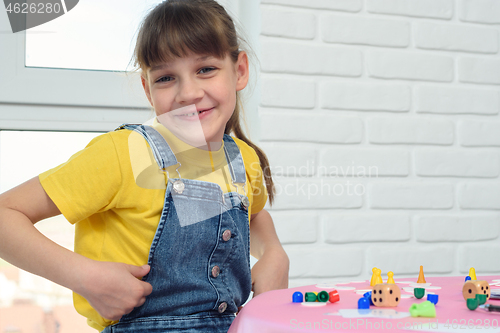 Image of A contented nine-year-old girl looked into the frame, sitting at the table and playing a board game