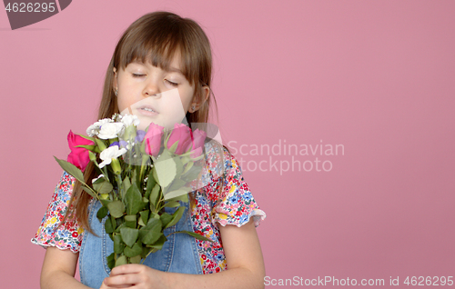 Image of Cute smiling adorable child girl holding bouquet of spring flowers isolated on pink background