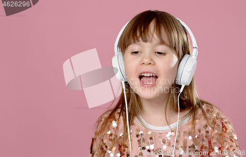 Image of Pretty 6 or 7 years old little girl singing and dancing with headphones