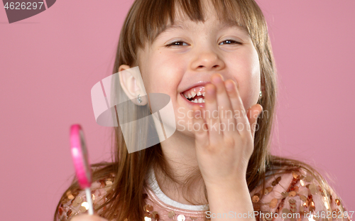 Image of Adorable young girl posing with pink lollypop candy. Smiling to the camera with all happyness