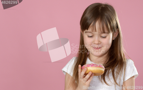 Image of Studio portrait of a beautiful little girl holding a donut and smelling tasty flavour