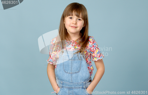 Image of Cute little girl standing in dungarees jeans with hands in pockets