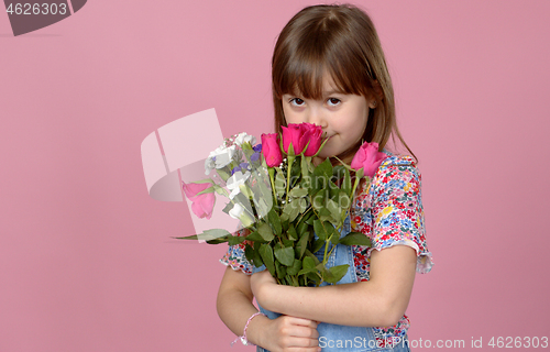 Image of Sweet adorable young little girl holding bunch of fresh spring flowers. Wearing dungarees