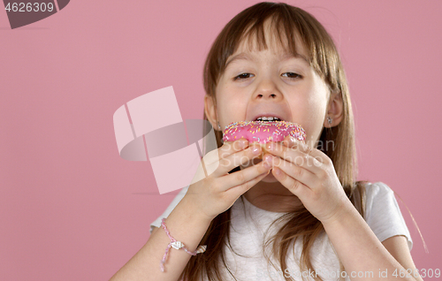 Image of Cute young caucasian girl caught eating a sweet pink doughnut