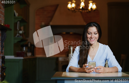 Image of Smiling woman sitting and table and using smartphone